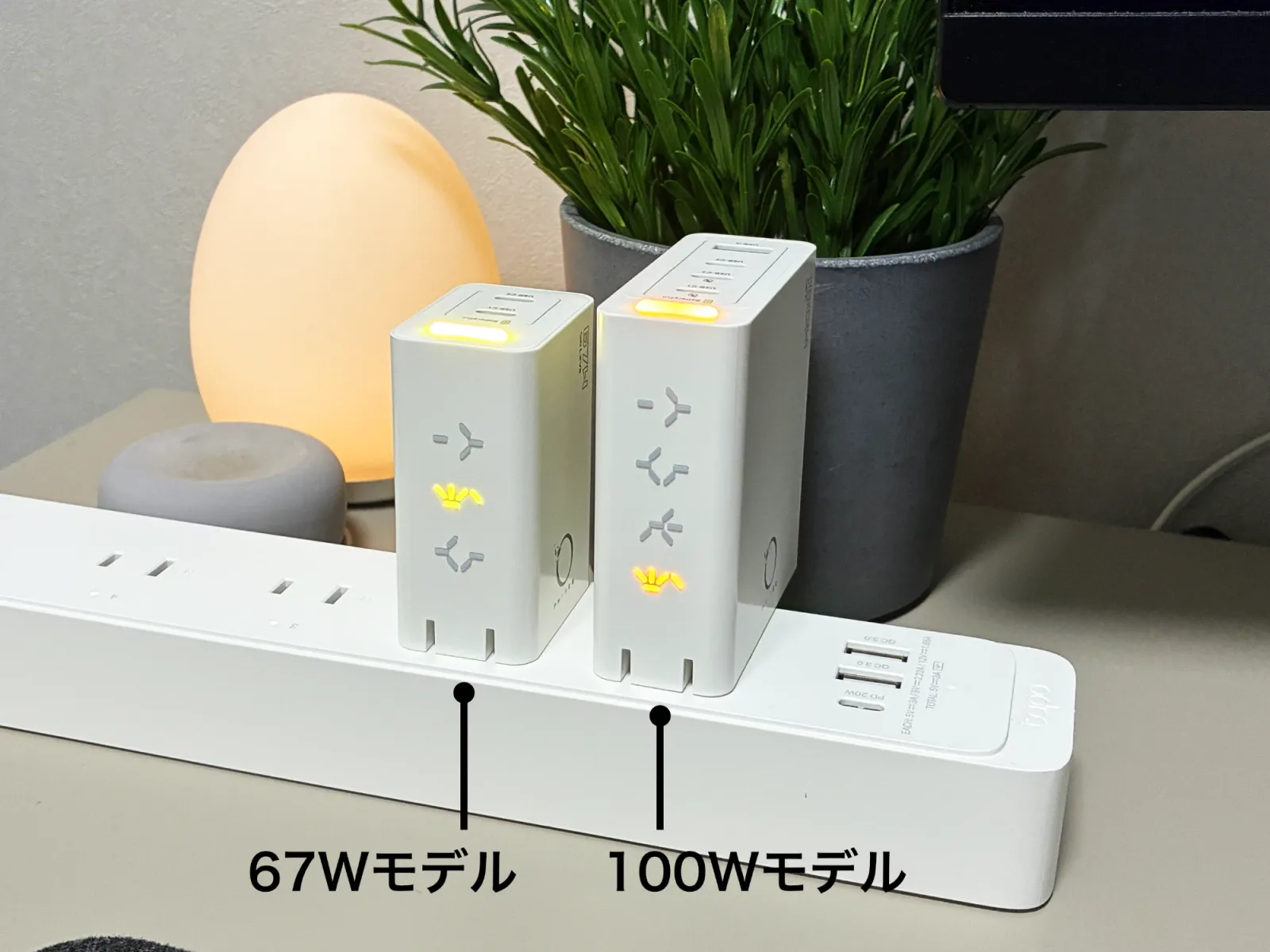 電源タップの隣り合う差込口に、PHYSCE 67W（左）と100W（右）を並べて挿したところ。100Wは67Wより背が高く奥行きもあるが、タップの上で使う幅は同じくらいで、2台がぶつからずに並んでいる