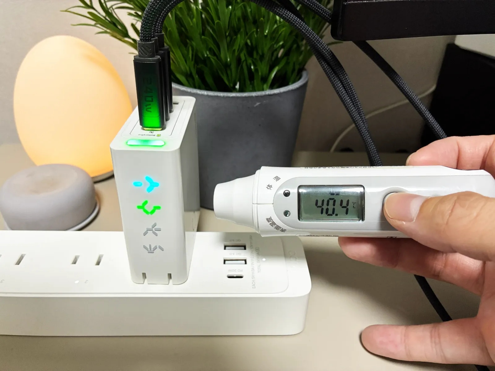 電源タップに挿してケーブルを3本つないだPHYSCE 100Wに、非接触の温度計を向けているところ。温度計の表示は40.4℃