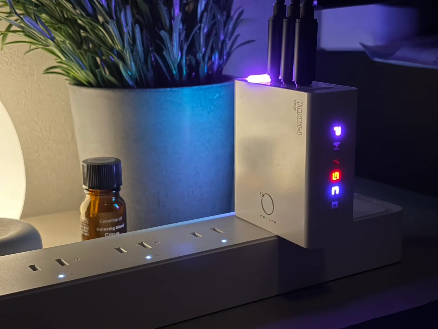 薄暗い部屋で電源タップに挿したPHYSCE 100W。上面のライトと、側面に縦に並んだPHYSCEの文字が青や赤に光っている